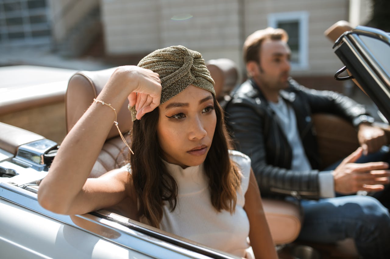 Woman looking distressed while sitting in a convertible with a man in the background, symbolizing emotional distance and red flags in relationships.