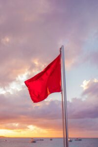 Red flag on beach at sunset with boats by the horizon
