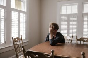 A man sitting by the dining table while holding his head with his hand