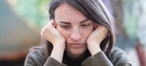 Woman resting her face in her hands, looking down with a sad, tired expression.