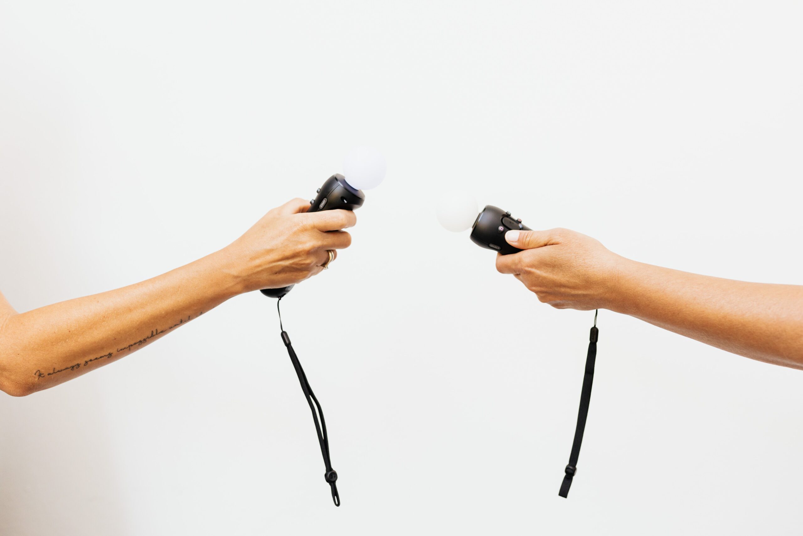 Two hands hold black handheld devices with white light bulbs on top, facing each other against a white background.